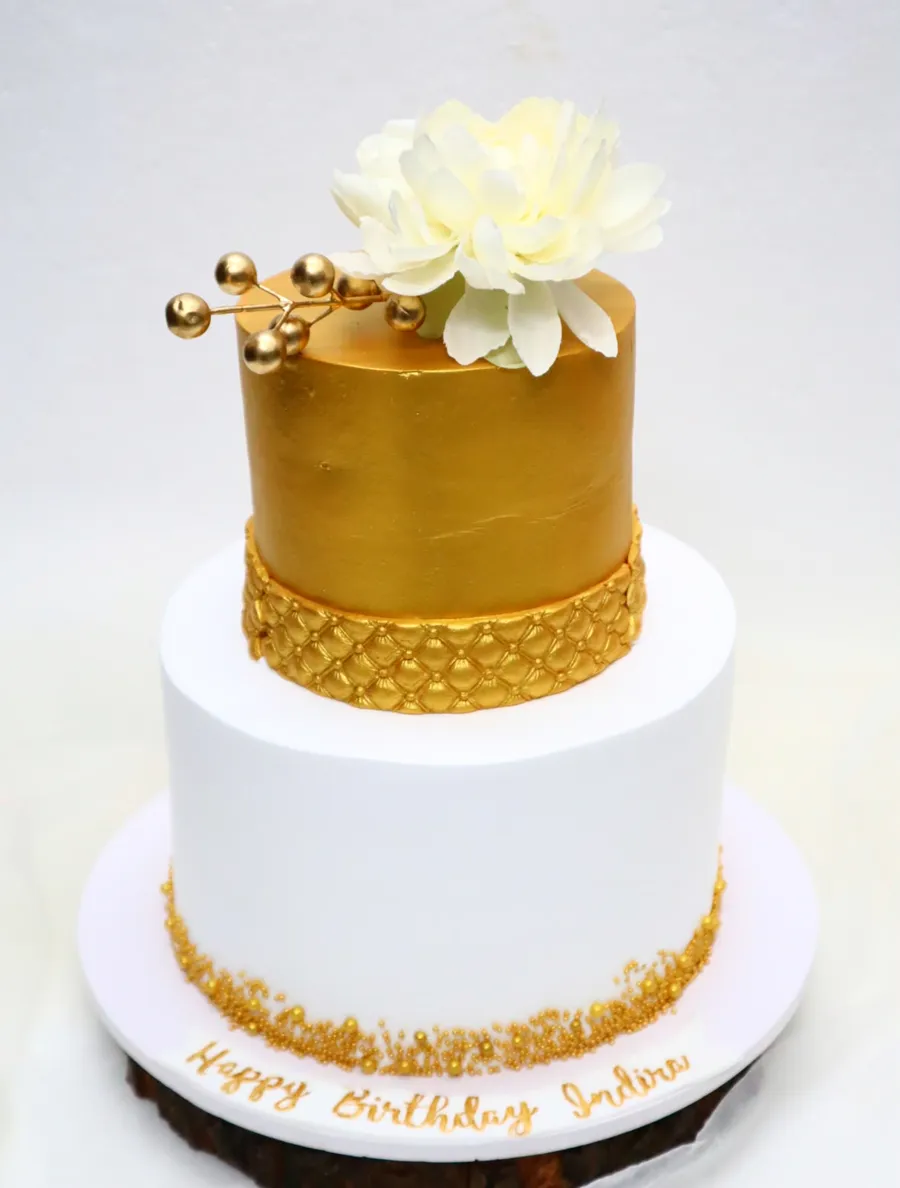 Gold and white two-tier birthday cake with a sugar flower