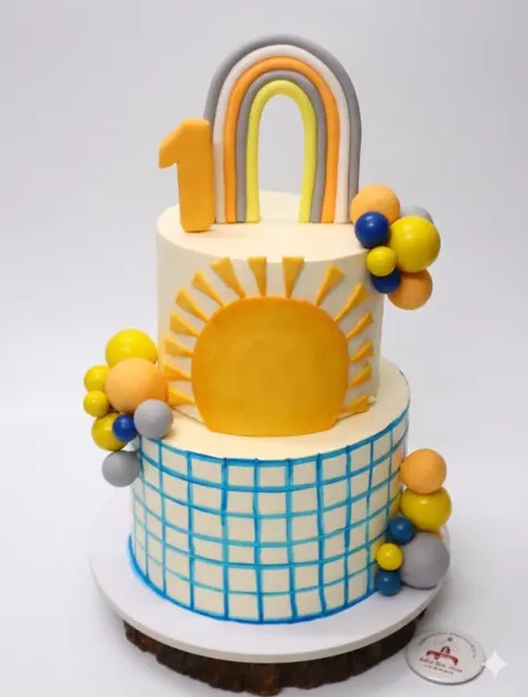 Two-tier 10th birthday cake with a rainbow, sun and balloons