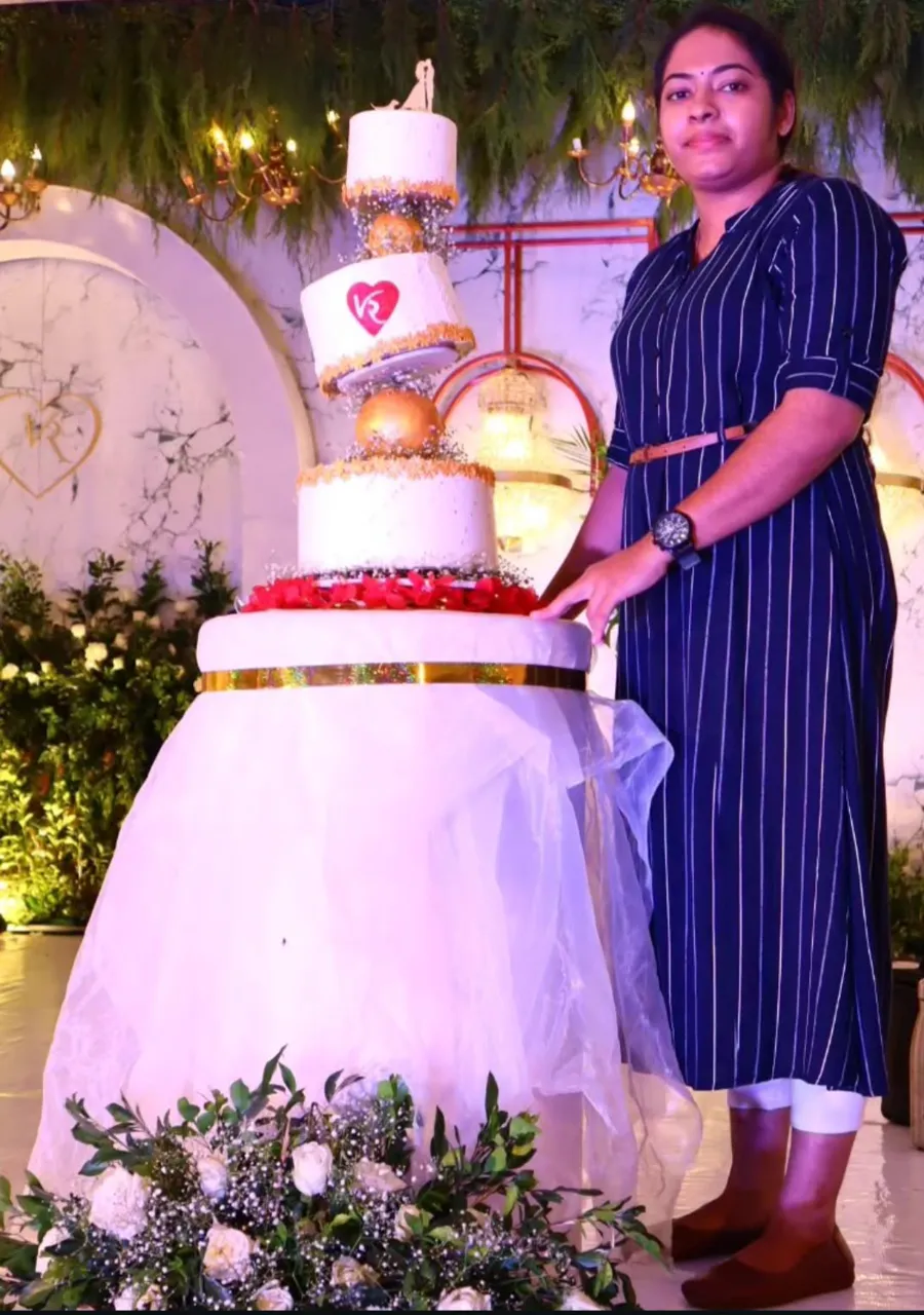 Athira Anoop, founder of Adhi's Bake House, with a tall multi-tier wedding cake